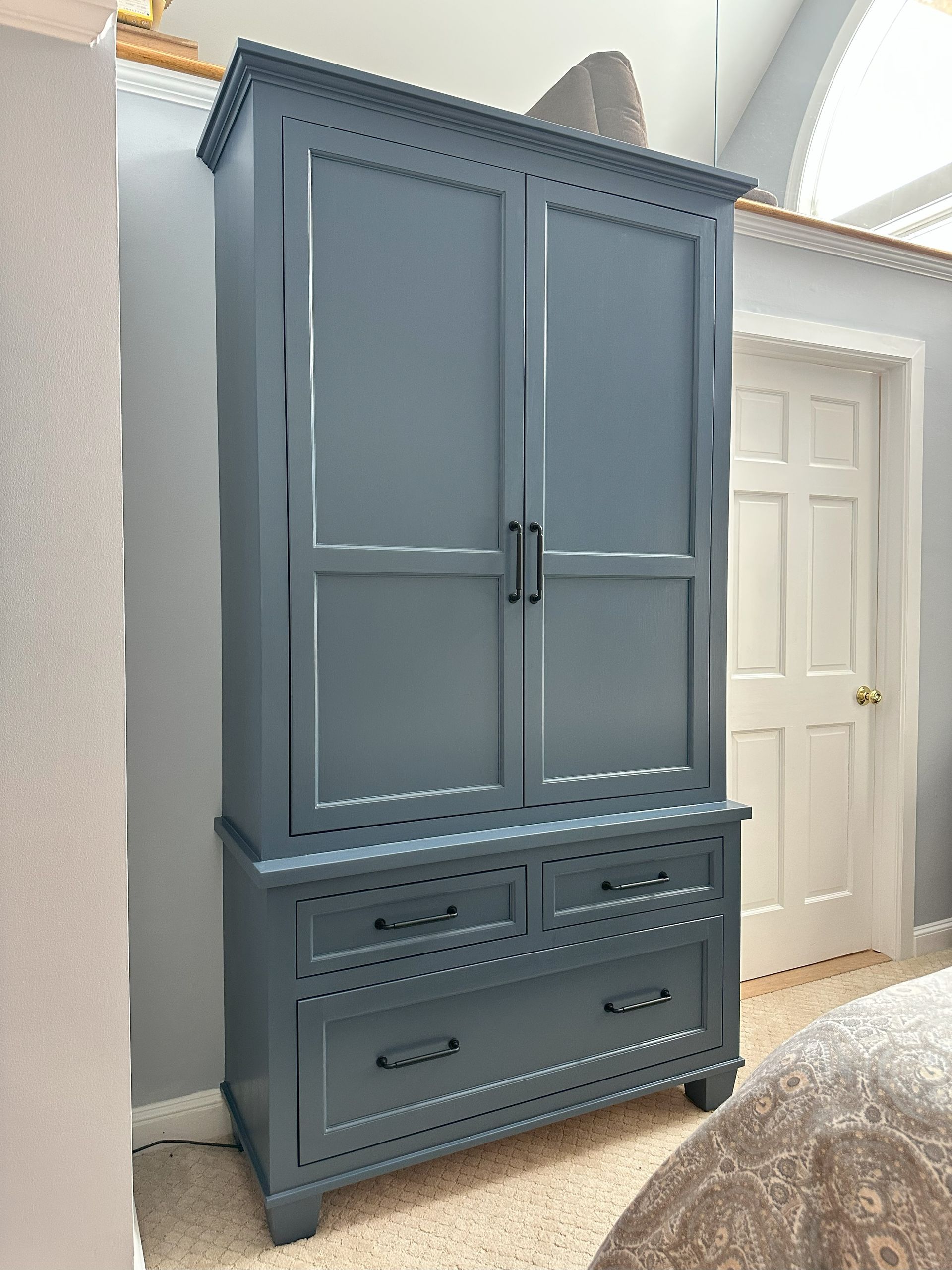 A large gray cabinet is sitting in a bedroom next to a bed.