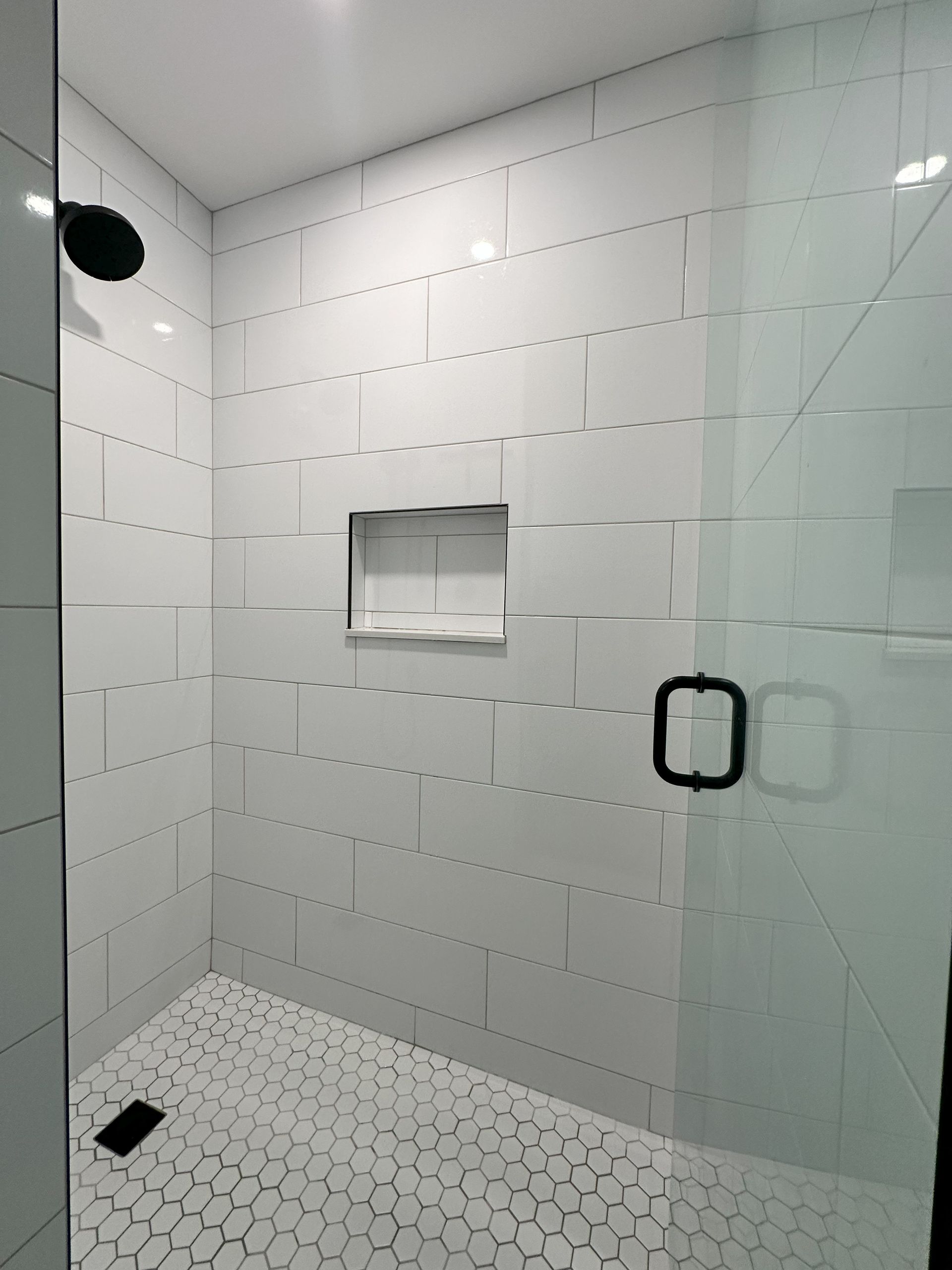 A walk in shower with white tiles and a black shower head.