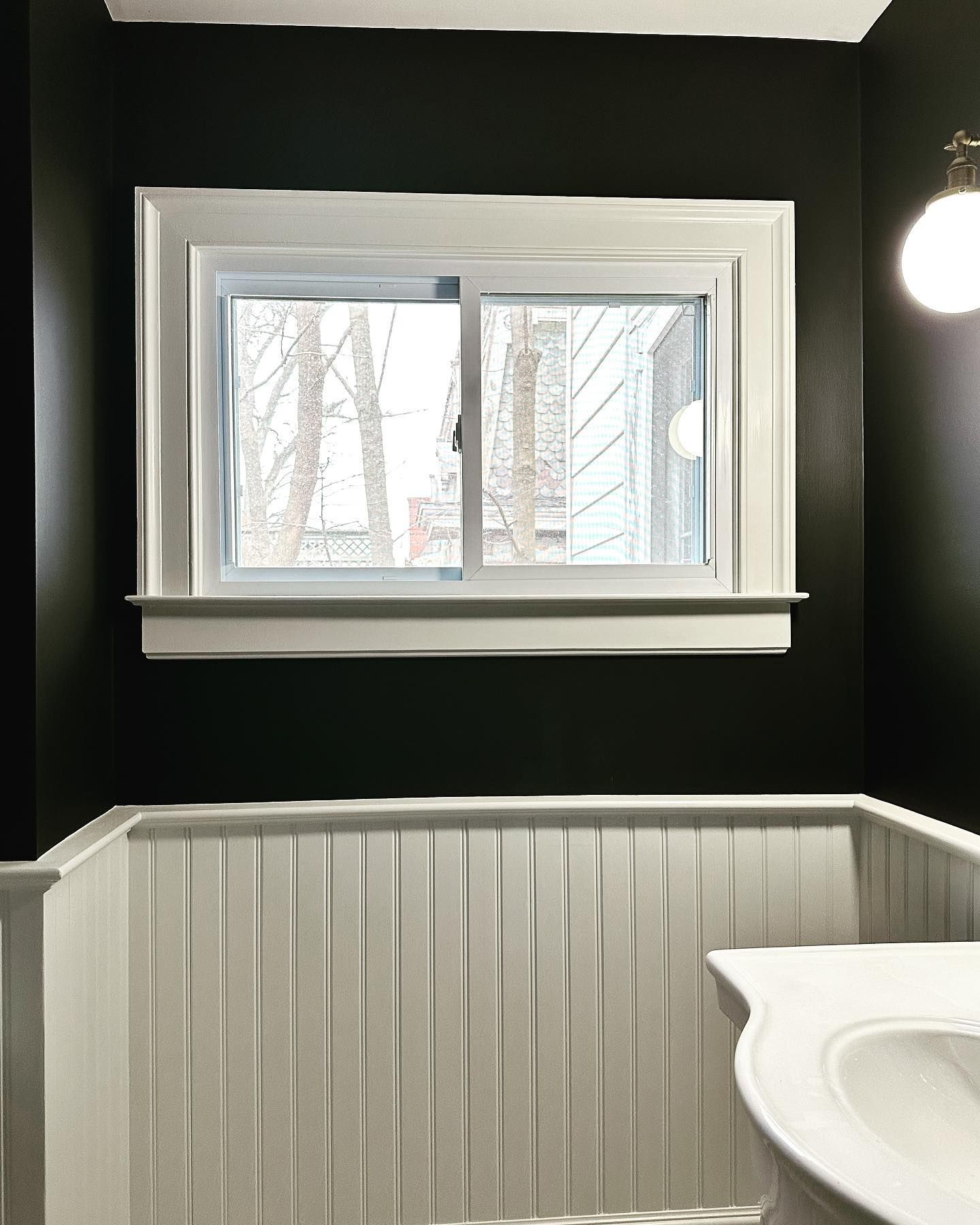 A bathroom with black walls , a sink , and a window.