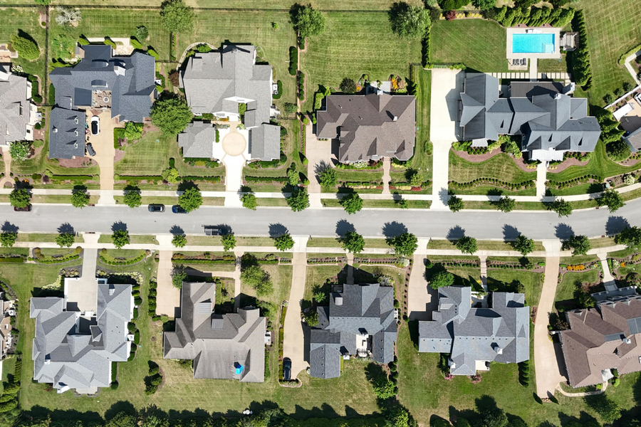 Aerial view of a suburban neighborhood with houses, tree-lined streets, and a backyard swimming pool.