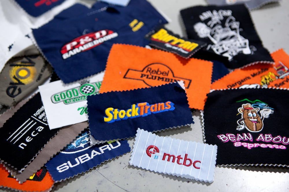 Pile of embroidered patches with company logos in various colours — Workwise Clothing Forster in Forster, NSW