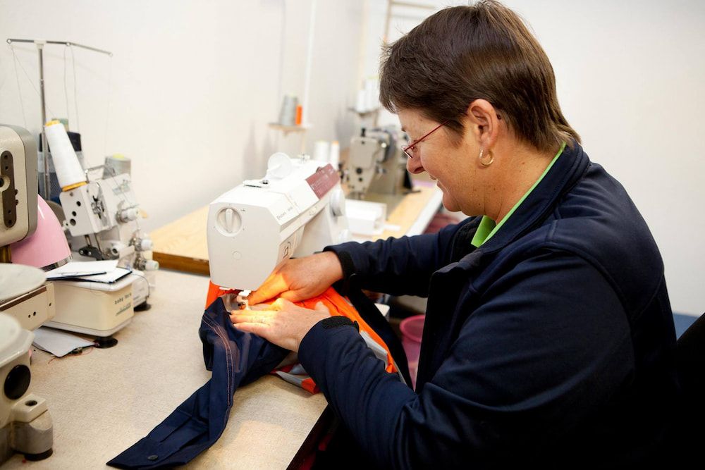 Woman Sewing at a Sewing Machine in a Brightly Lit Room — Workwise Clothing Forster in Taree, NSW