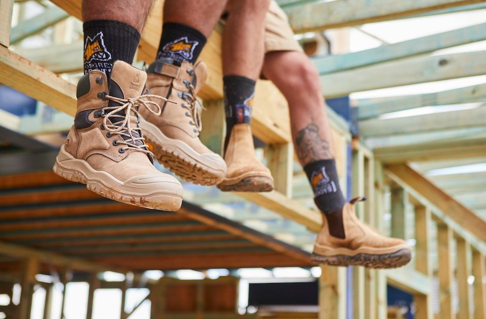Two People Wearing Work Boots and Socks With Construction Site Logo — Workwise Clothing Forster in Wingham, NSW