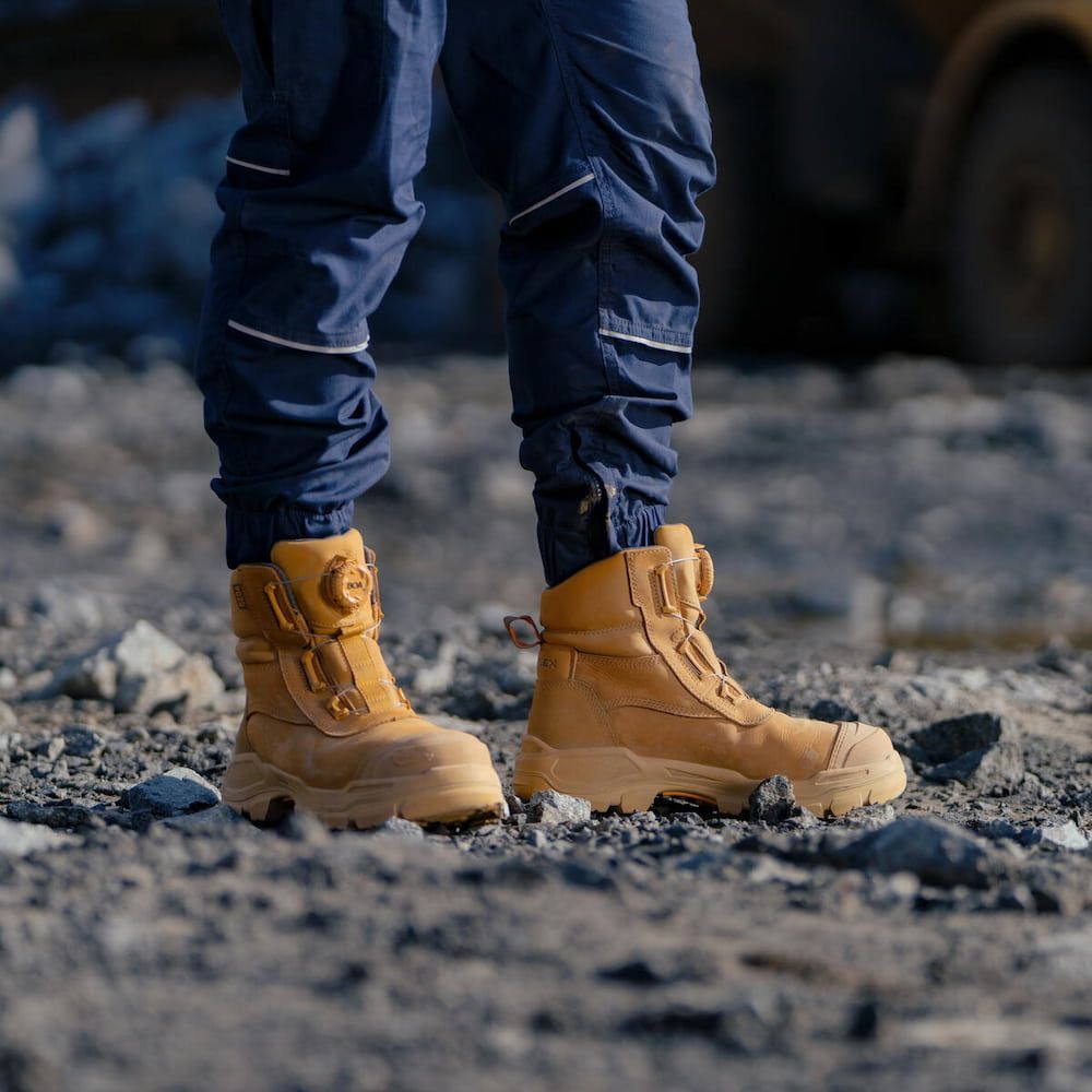 Person in Tan Work Boots and Blue Work Pants Stands on Gravel — Workwise Clothing Forster in Taree, NSW