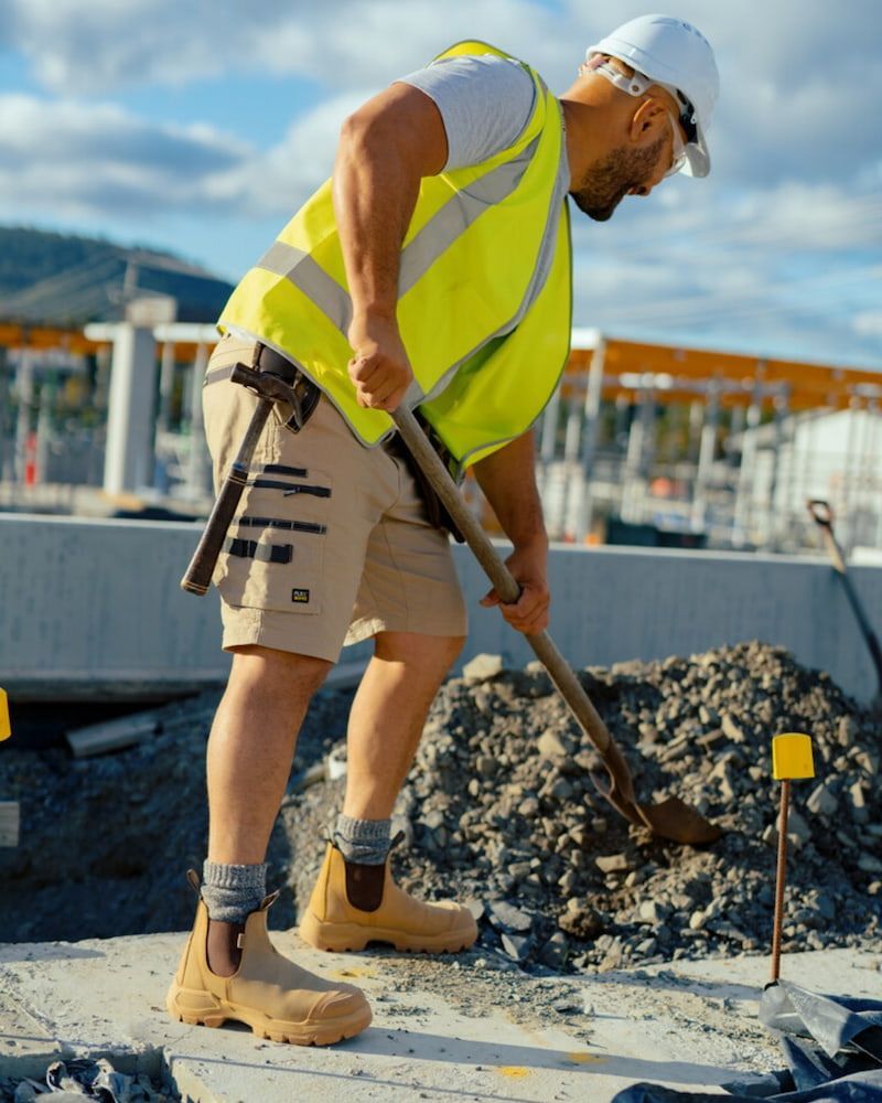 Construction Worker in Safety Vest and Hard Hat Digs With a Shovel Outdoors — Workwise Clothing Forster in Forster, NSW