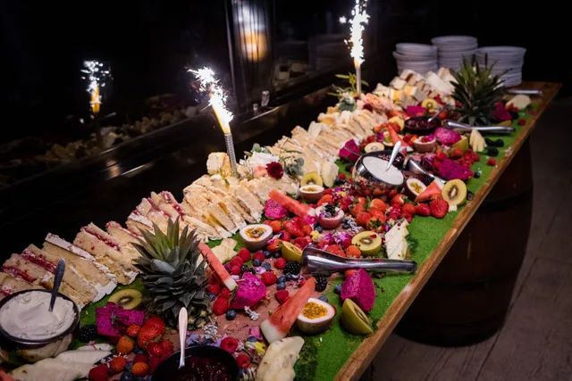 A long wooden table topped with a variety of fruits and sandwiches.