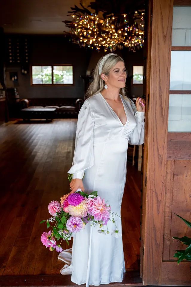 A woman in a white dress is standing in a doorway holding a bouquet of flowers.