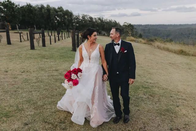A bride and groom are walking in a field holding hands.