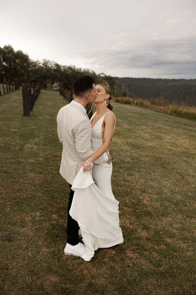 A bride and groom are kissing in a grassy field.