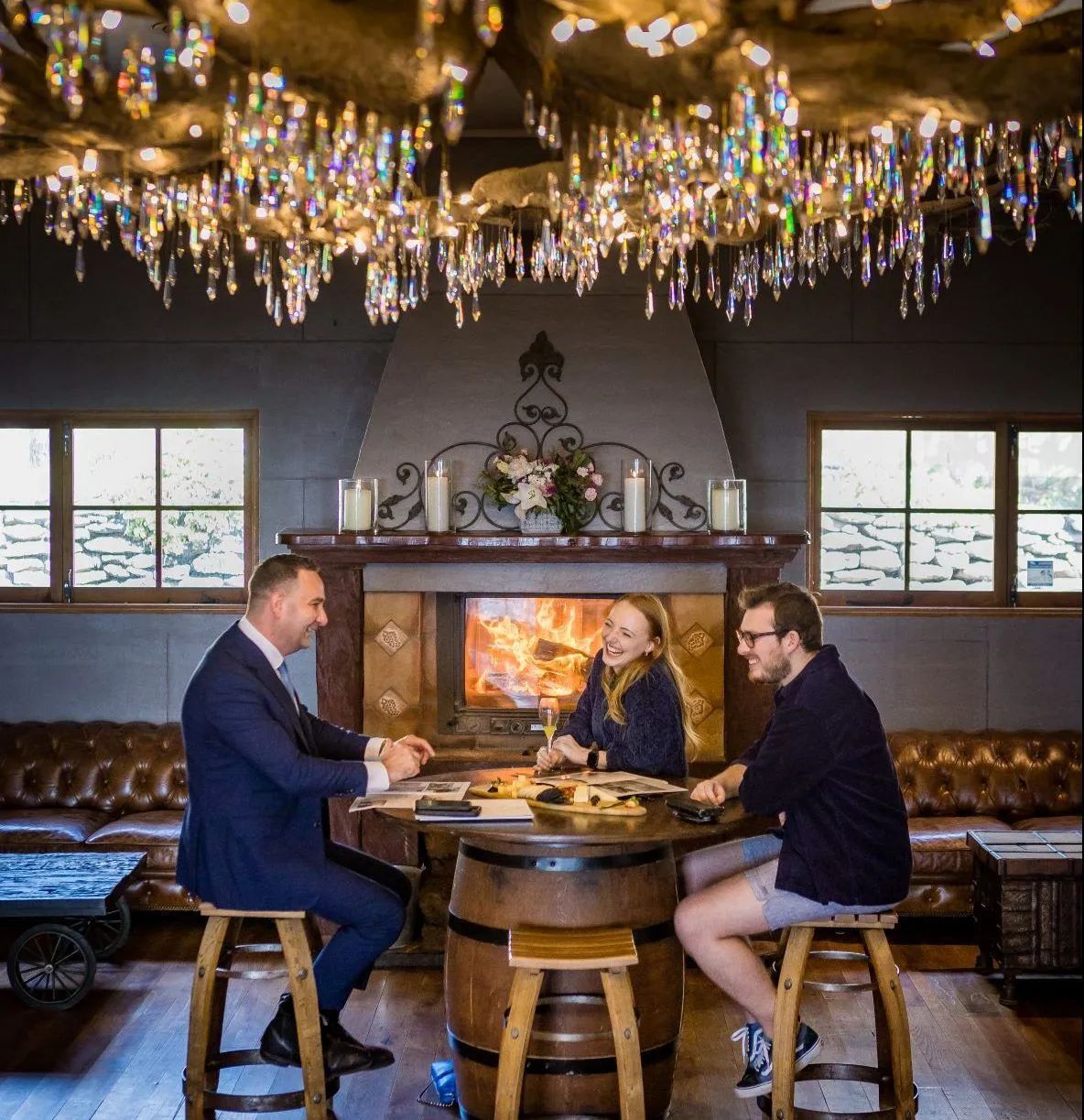 Three people are sitting at a table in front of a fireplace