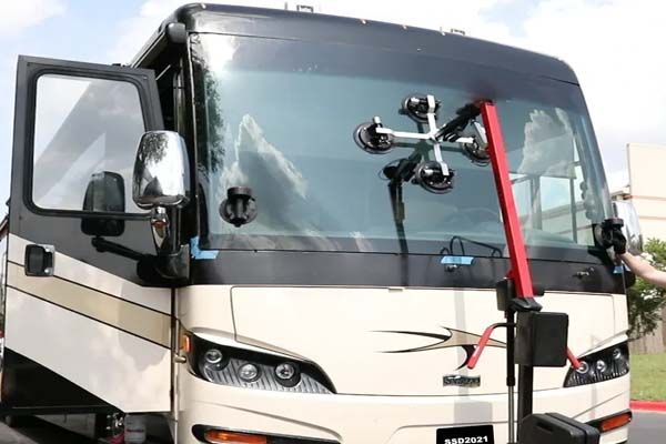 A rv with a windshield being replaced by a person.