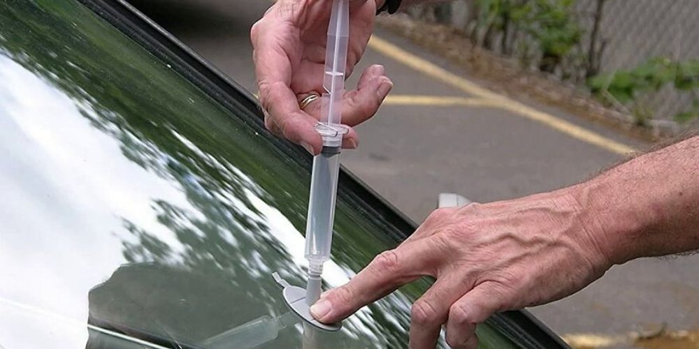 Rock Chop  Repair A person is holding a syringe in front of a car window.