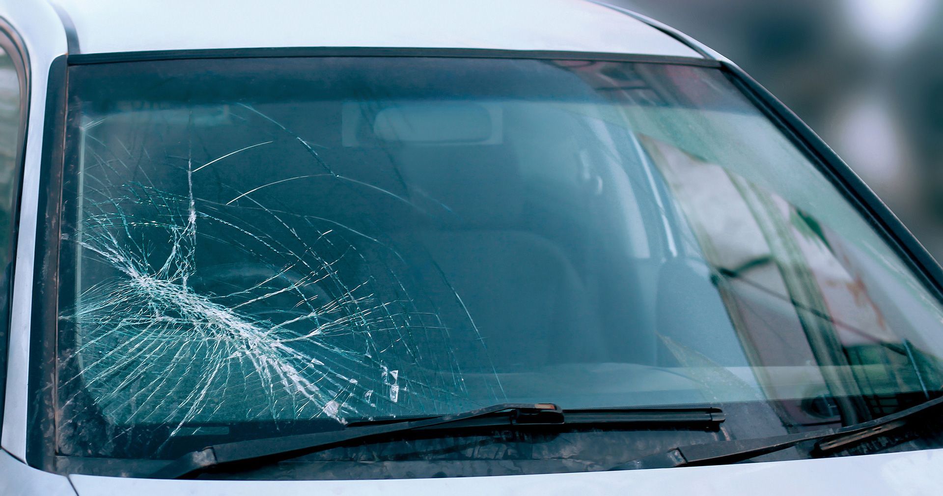 A white car with a broken windshield is parked on the side of the road.
