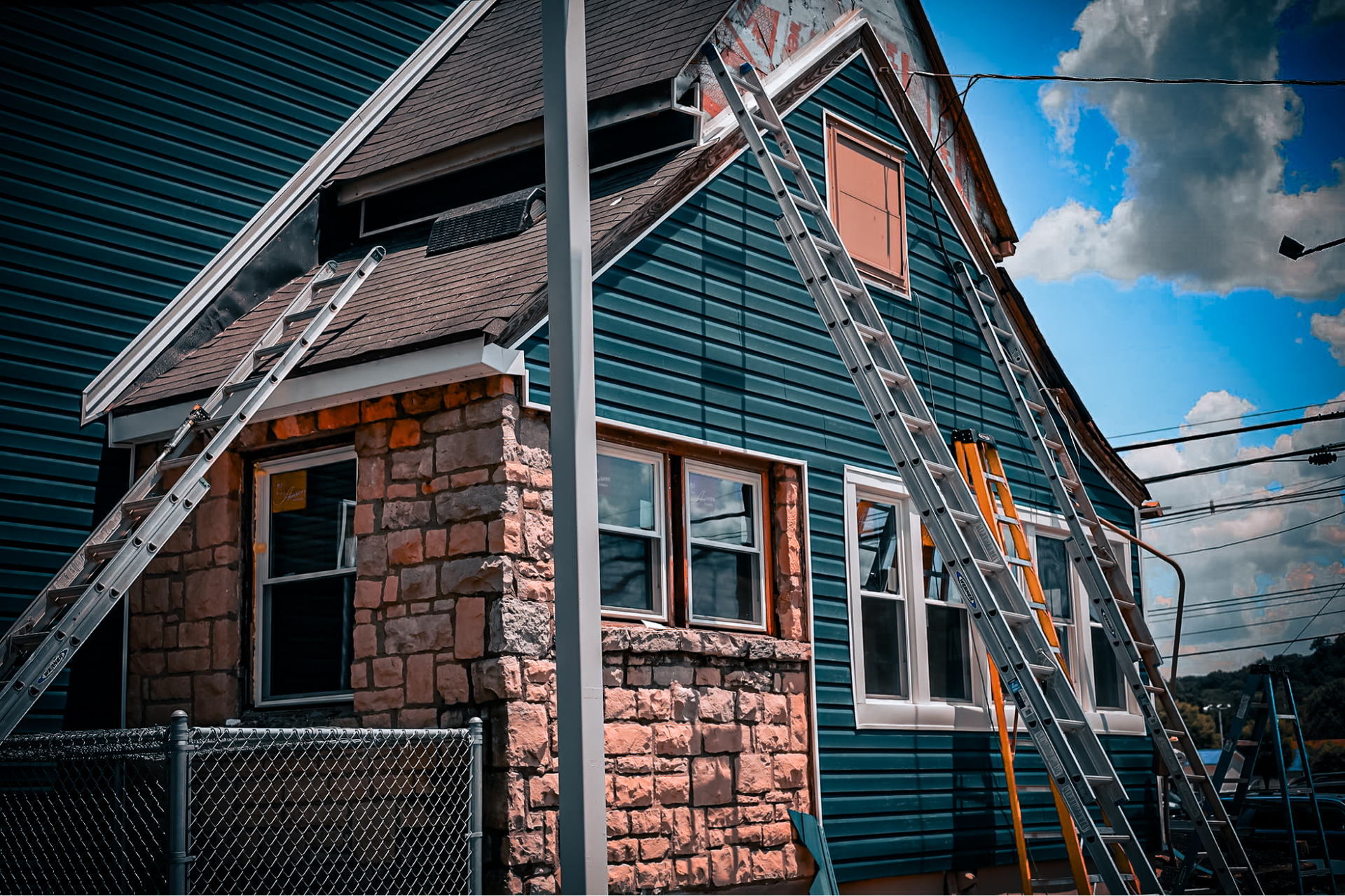 House with blue siding and brick accents; ladders propped up for construction against a blue sky.