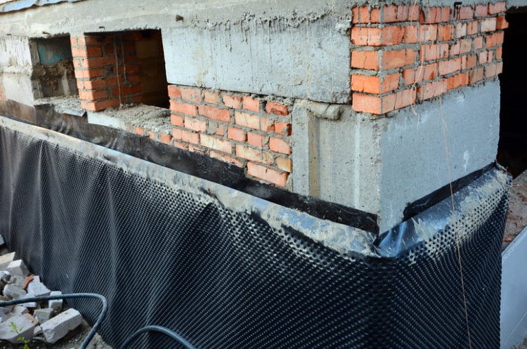 Workers stabilizing sinking house foundation with concrete leveling equipment