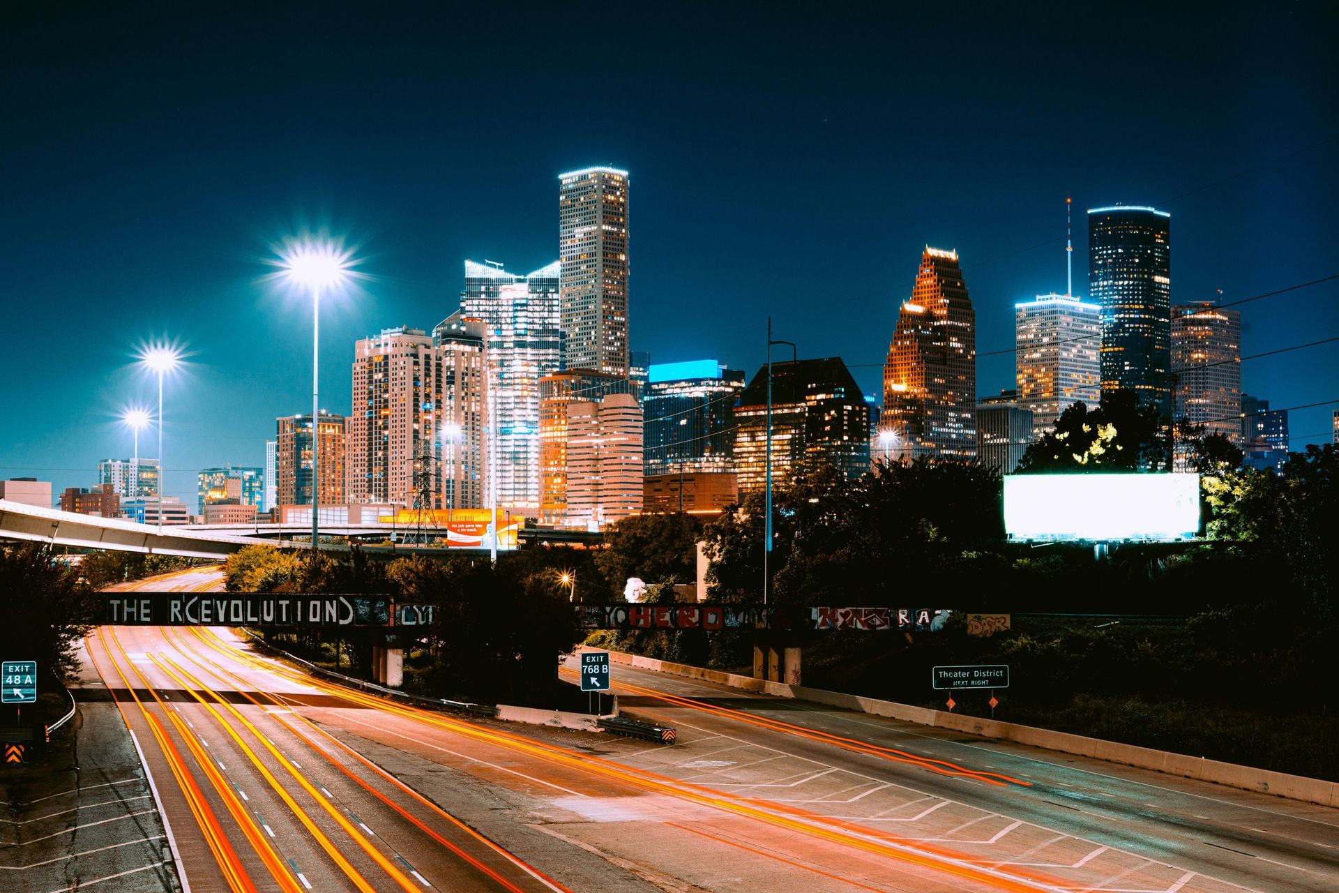 Houston, Tx nighttime city skyline with illuminated skyscrapers above a light-streaked highway