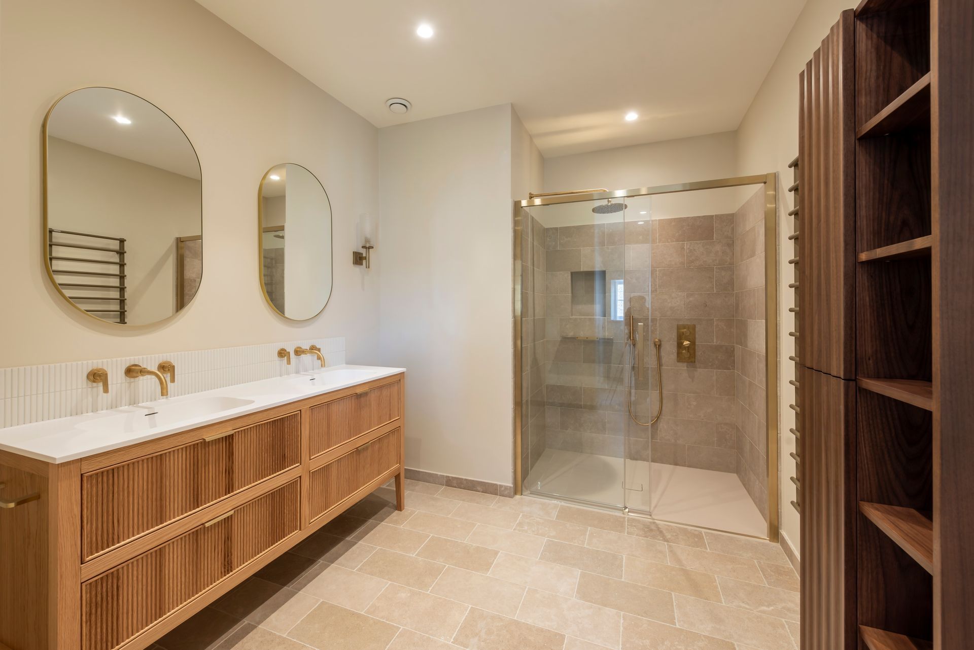Modern bathroom with double vanity, oval mirrors, wood cabinetry, and glass shower doors
