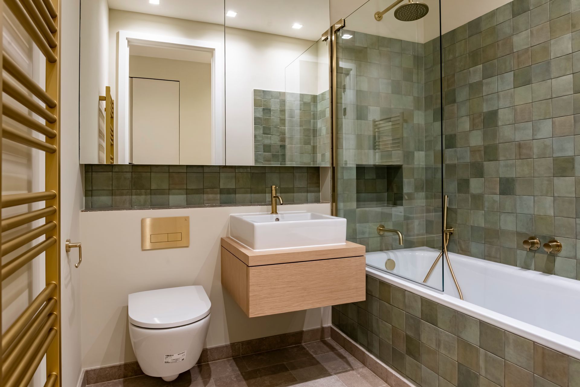 Modern bathroom with green tile walls, glass shower, wall-mounted sink, toilet, and mirror