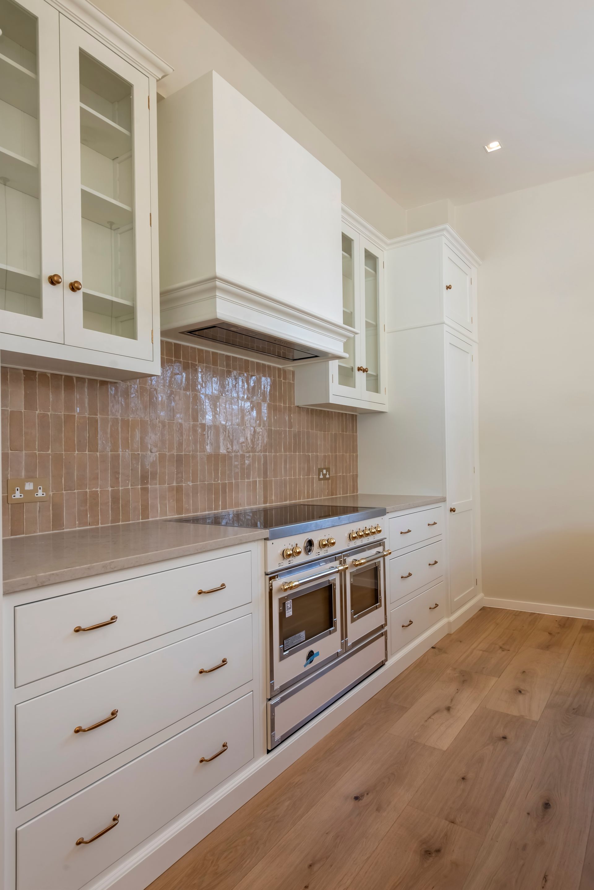 Modern white kitchen with wood floors, marble-look counters, beige tile backsplash, and stainless steel stove.