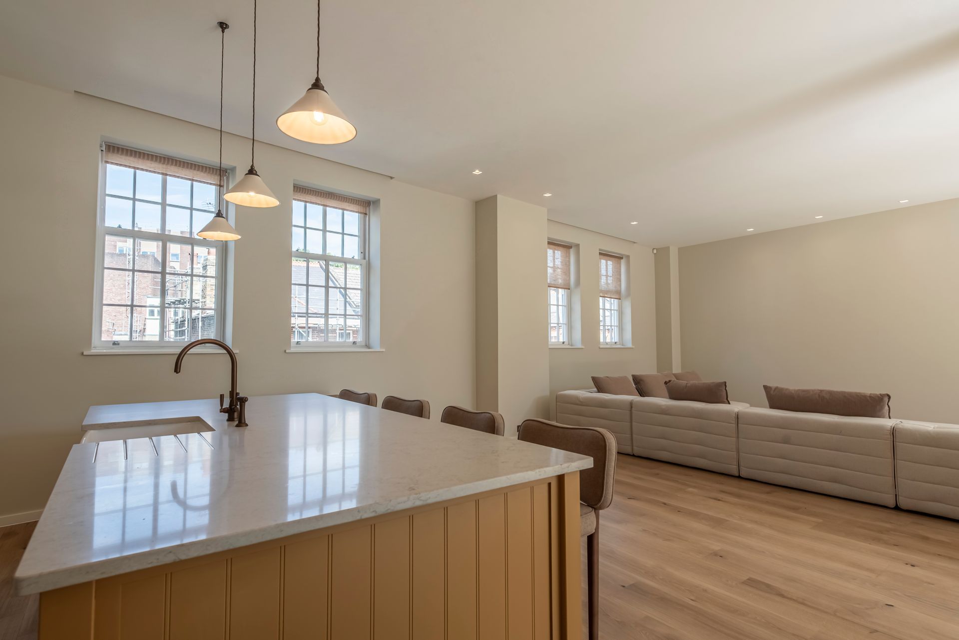 Bright open-plan kitchen and living room with island, pendant lights, beige sofa, and large windows