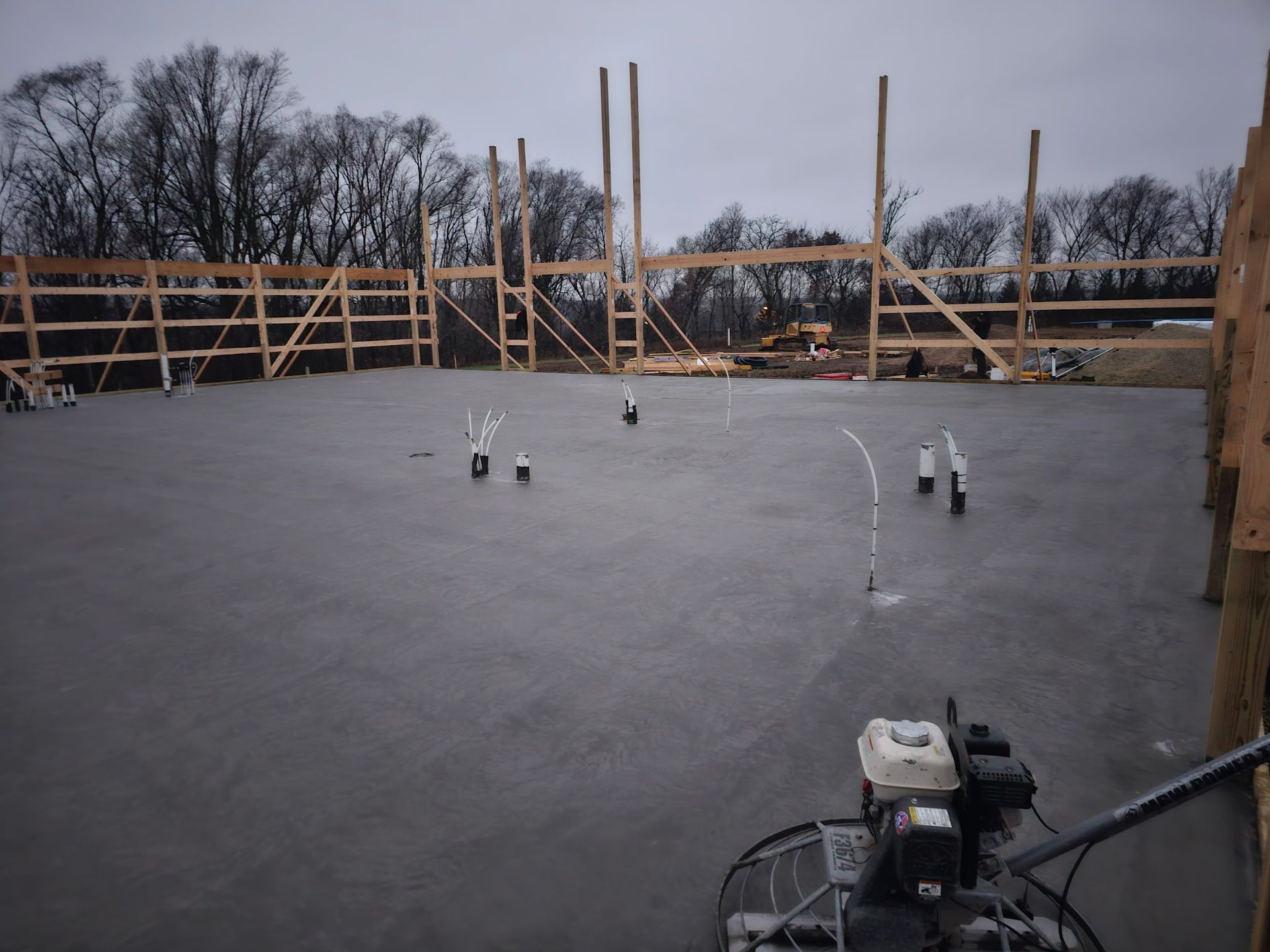 Newly poured concrete floor with wooden framing in progress, overcast sky.