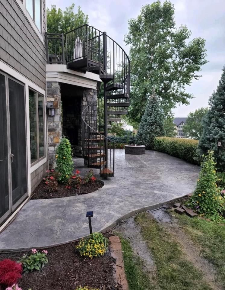 Outdoor patio with a spiral staircase leading to a second level. Grey stamped concrete path, small garden, and fire pit.