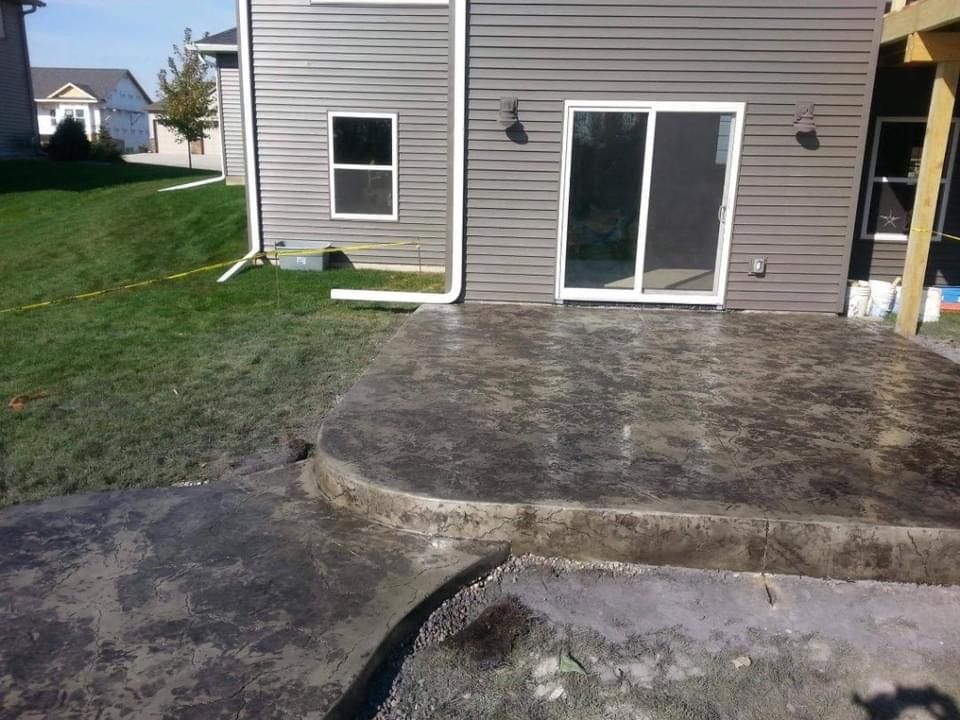 Concrete patio with textured surface next to a house with gray siding and sliding glass doors.