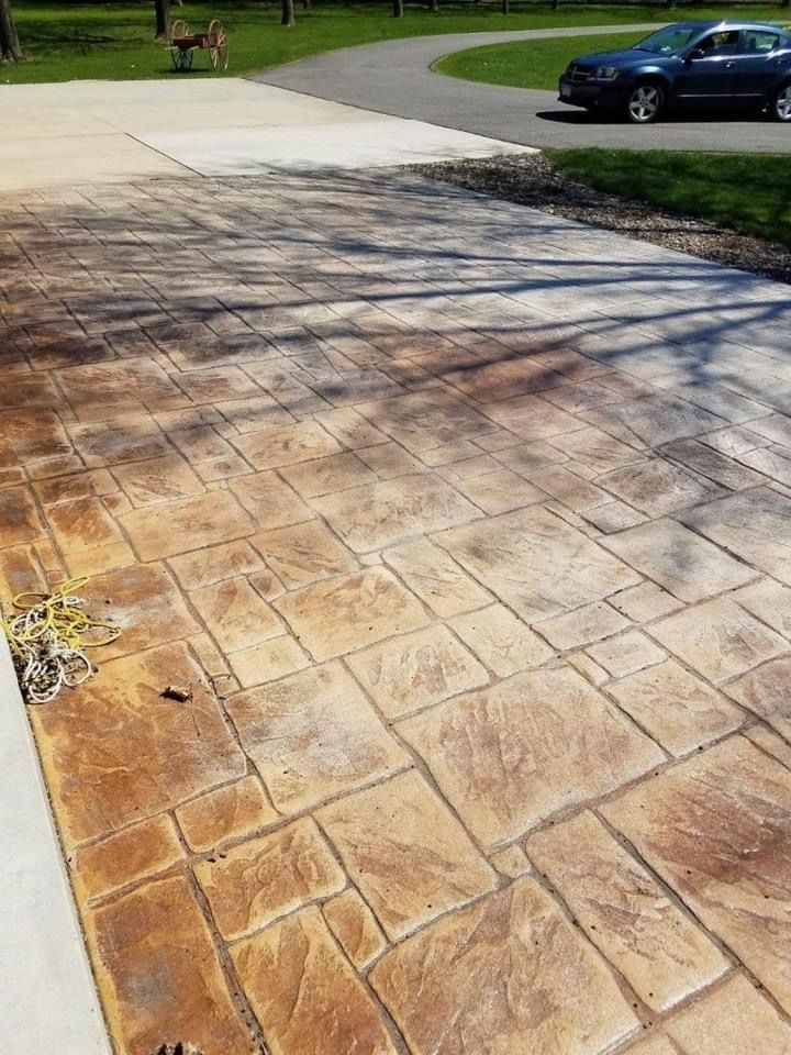 Stamped concrete driveway, brown and tan, in front of a house, with a car and a deer in the distance.