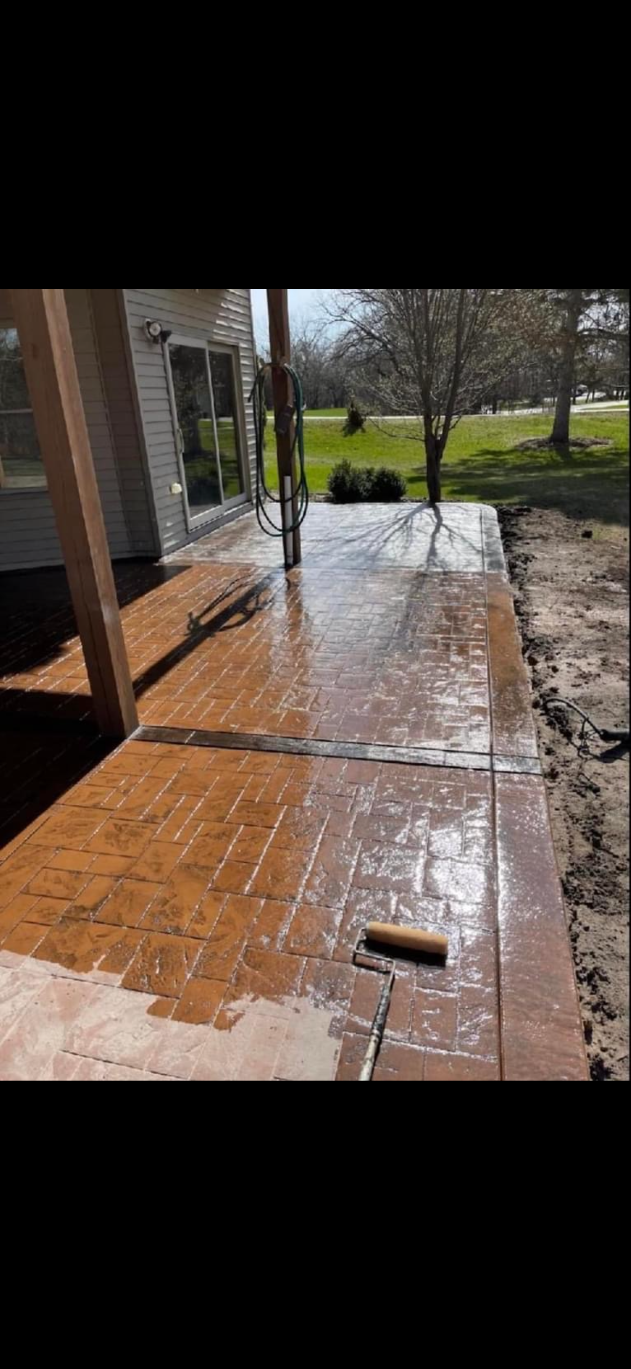 Wet concrete patio with brick pattern, being sealed. A roller is on the ground.