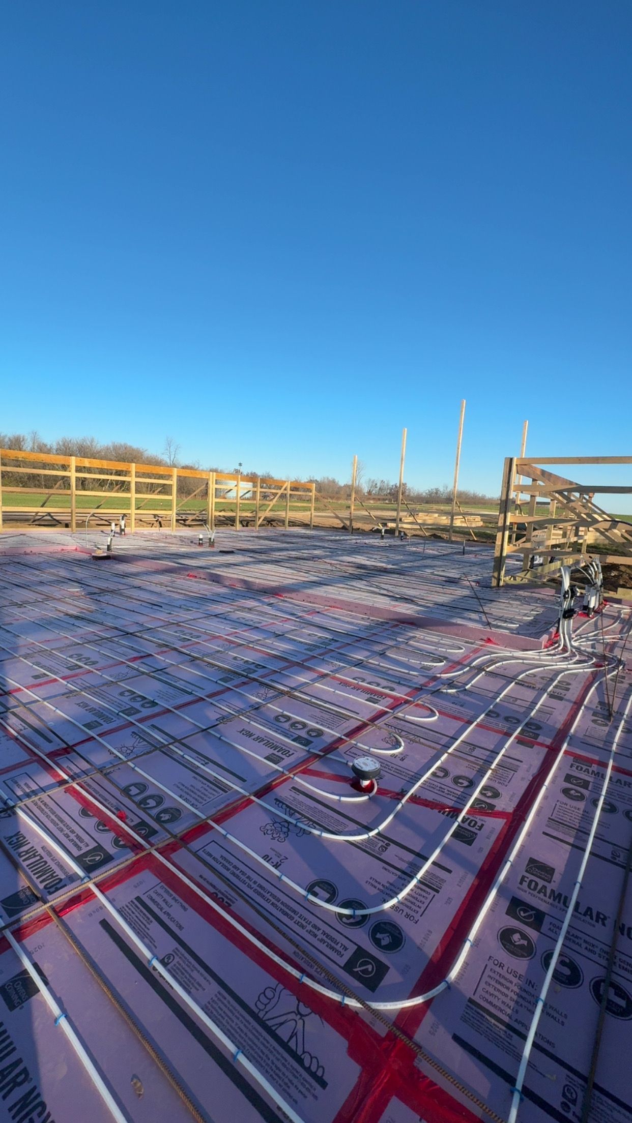 Radiant floor heating system installation with red tubing on pink insulation, against a blue sky.