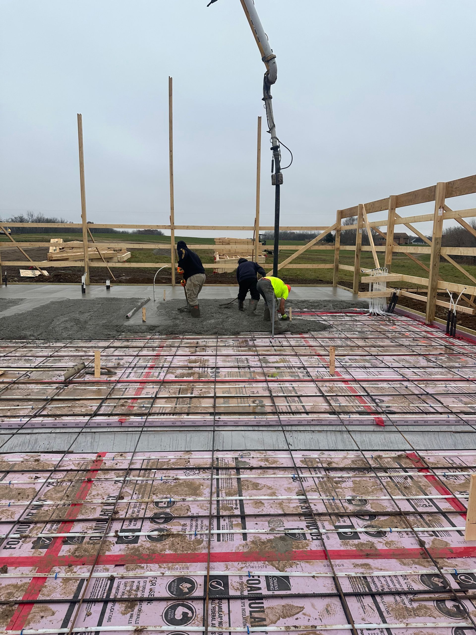 Construction workers pouring concrete on a foundation, using a pump truck. Cloudy day.