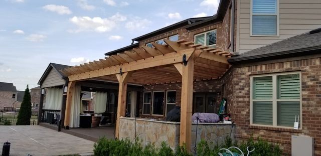 A wooden pergola covers a brick patio attached to a two-story house.