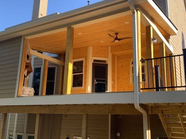 Wooden deck extension attached to a beige house with a ceiling fan, and supporting beams.