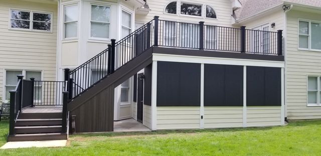 A multi-level deck with black railings and a screened-in lower level, attached to a light-colored house with windows.