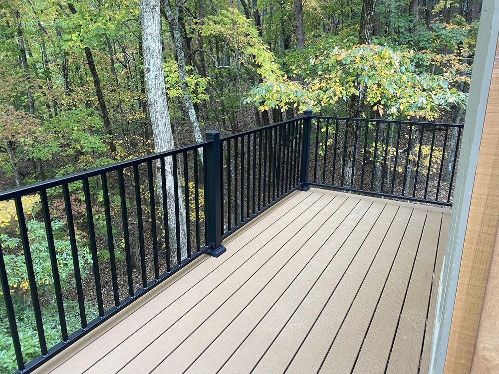 Wooden deck with black railing overlooks a forest. The deck has light brown planks.