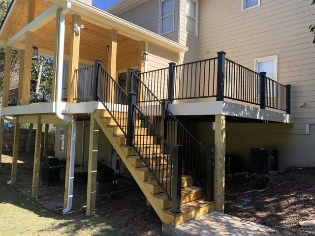 A multi-level deck with stairs and black railings attached to a two-story beige house.