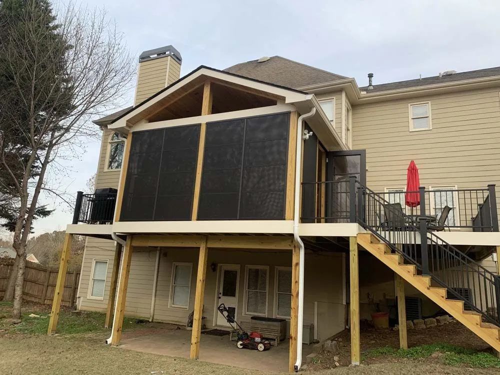 Screened-in porch attached to a two-story beige house with a wooden deck and stairs.