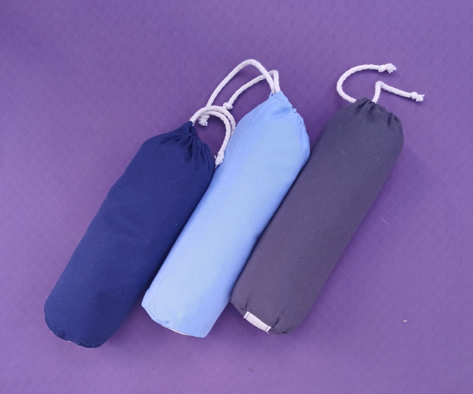 Tres esterillas de yoga enrolladas en azul marino, azul claro y gris sobre un fondo morado.