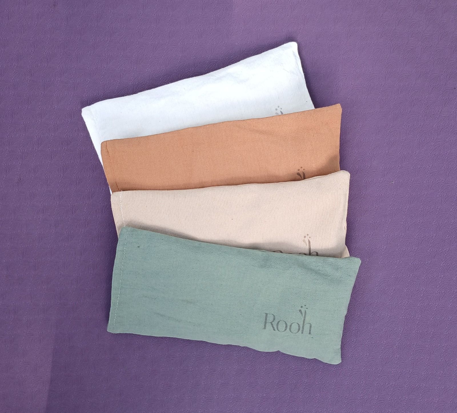Cuatro muestras de tela dobladas en blanco, tostado, beige y verde salvia sobre un fondo morado.