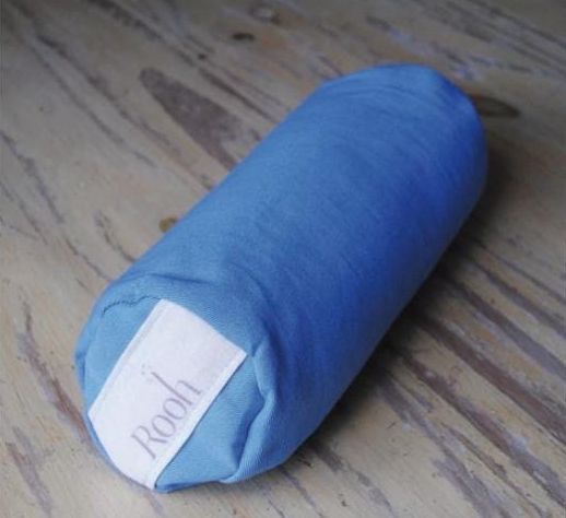 Cojín cilíndrico azul sobre un suelo de madera, con una etiqueta de tela blanca visible.