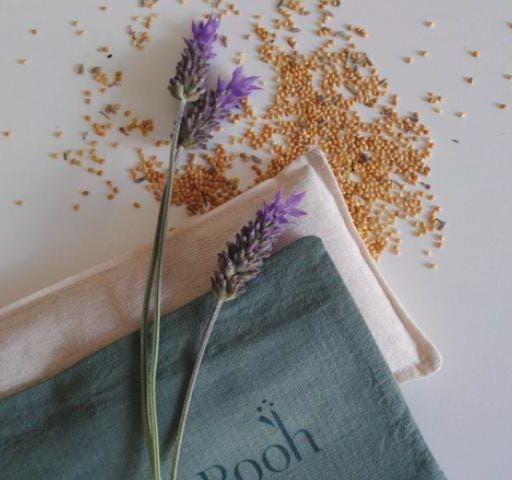 Flores moradas sobre una bolsita de tela beige con semillas esparcidas sobre una superficie clara.