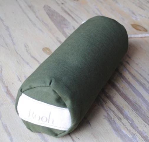 Estuche cilíndrico de tela verde con una etiqueta blanca en un extremo sobre una superficie de madera.