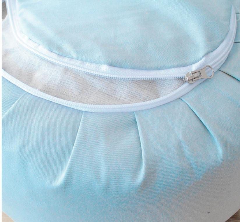 Cojín de satén azul claro con ribete de cremallera blanca y pliegues fruncidos.