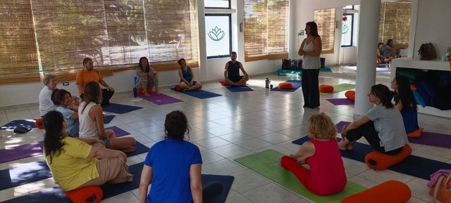 Mujer meditando sobre una esterilla de yoga en una habitación iluminada por el sol con texto sobre terapia de yoga y respiración suave.