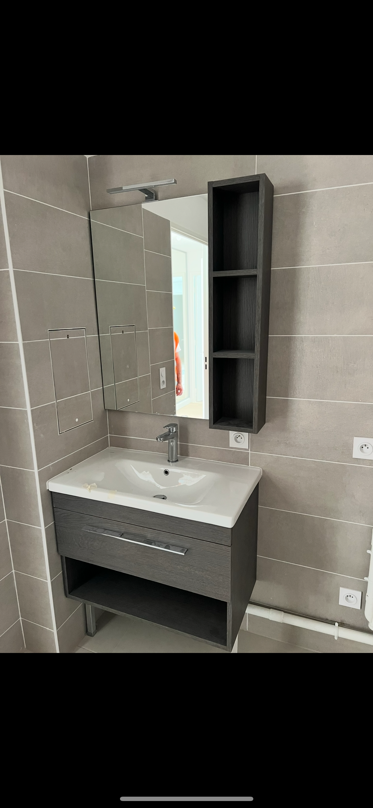 Meuble-lavabo moderne avec vasque, armoire à miroir, murs carrelés gris et petite étagère à serviettes.