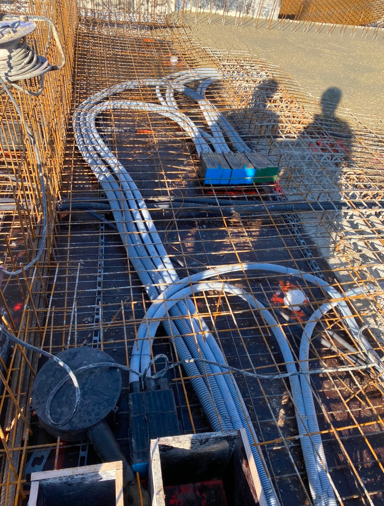 Câbles et conduits enroulés sur des barres d'armature sur un chantier de construction, avec un outil bleu dessus.