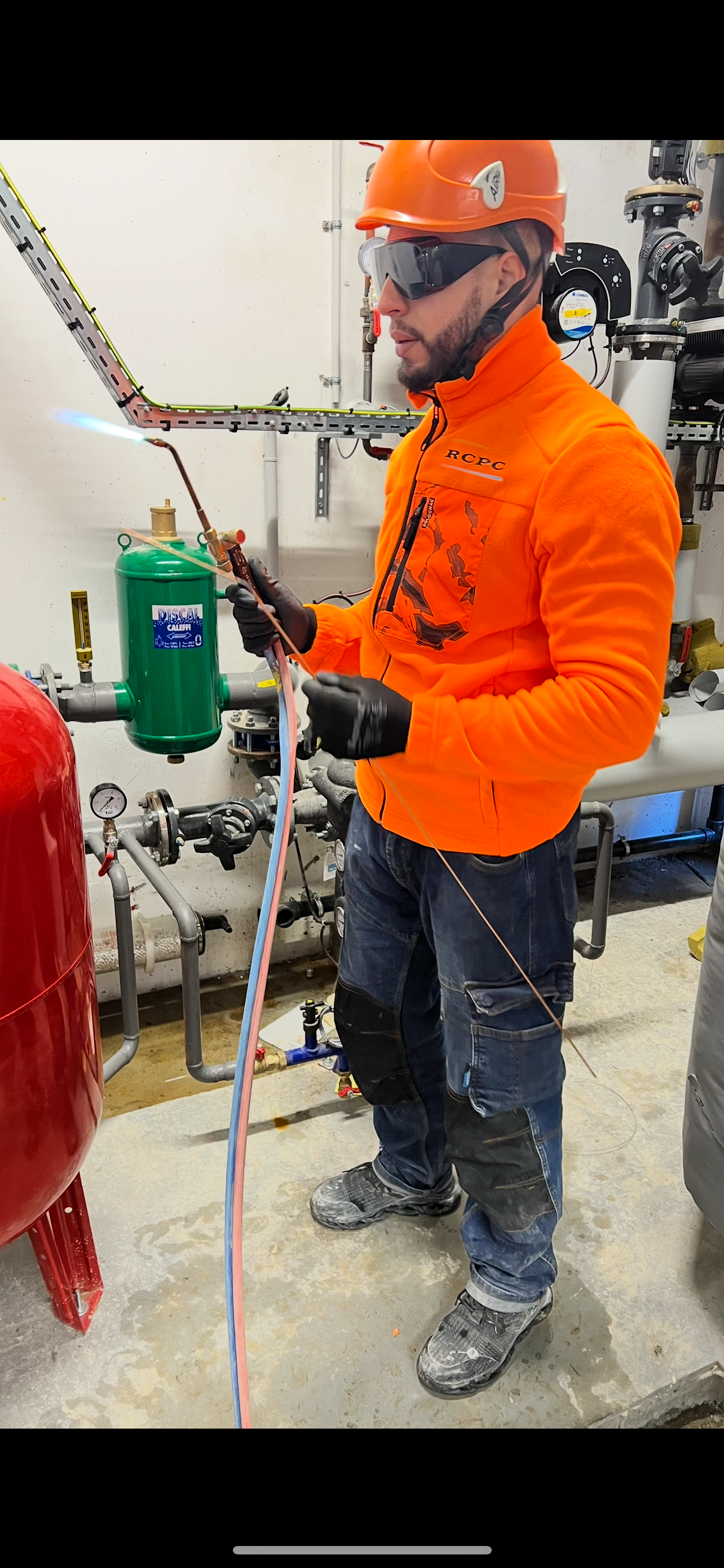 Ouvrier en tenue de sécurité orange manipulant du matériel dans une zone de travail industrielle.