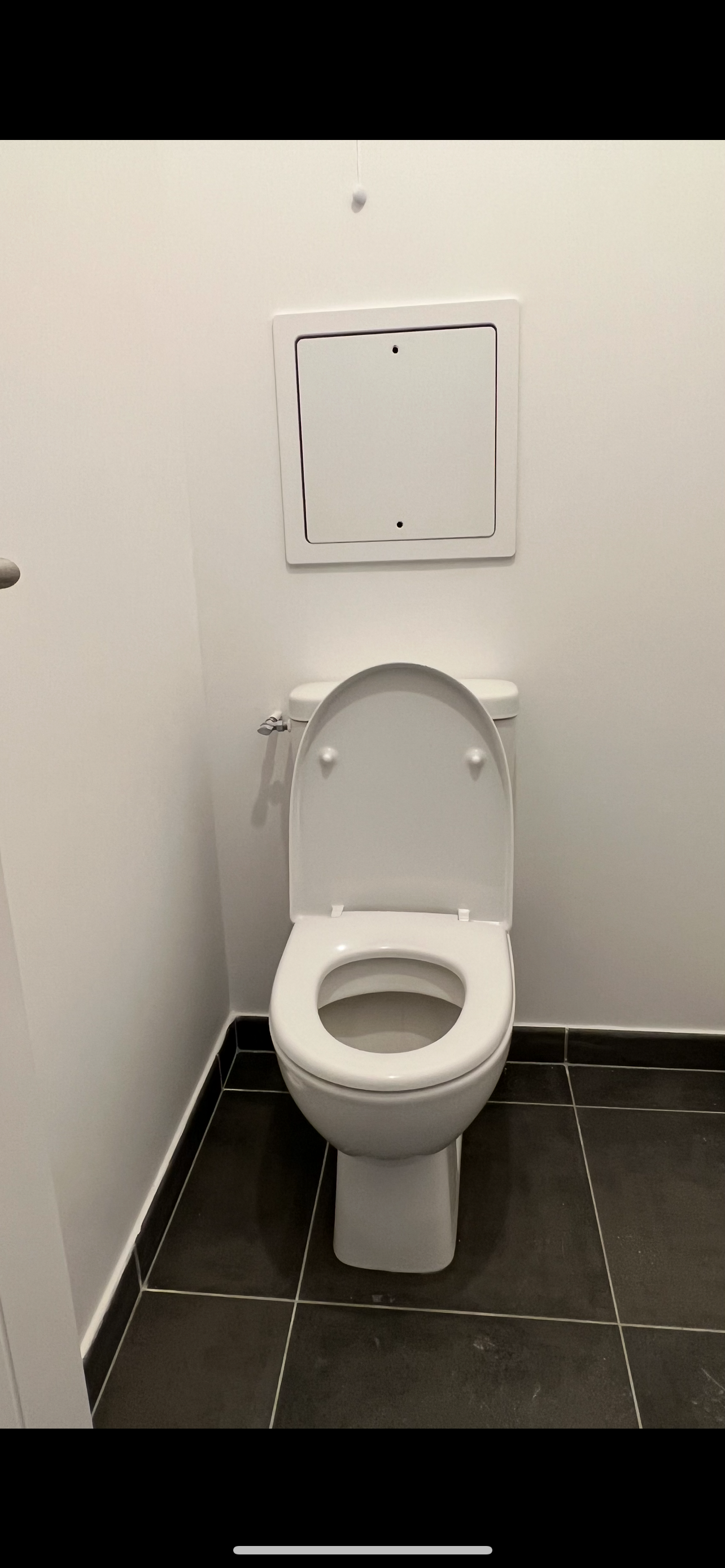 Petites toilettes avec des toilettes blanches contre un mur uni et un sol carrelé foncé.