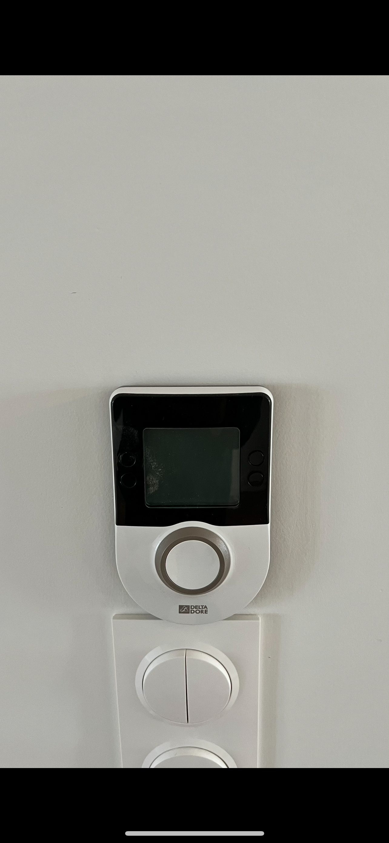 Thermostat mural avec petit écran noir et molette de réglage argentée, sur un mur clair.