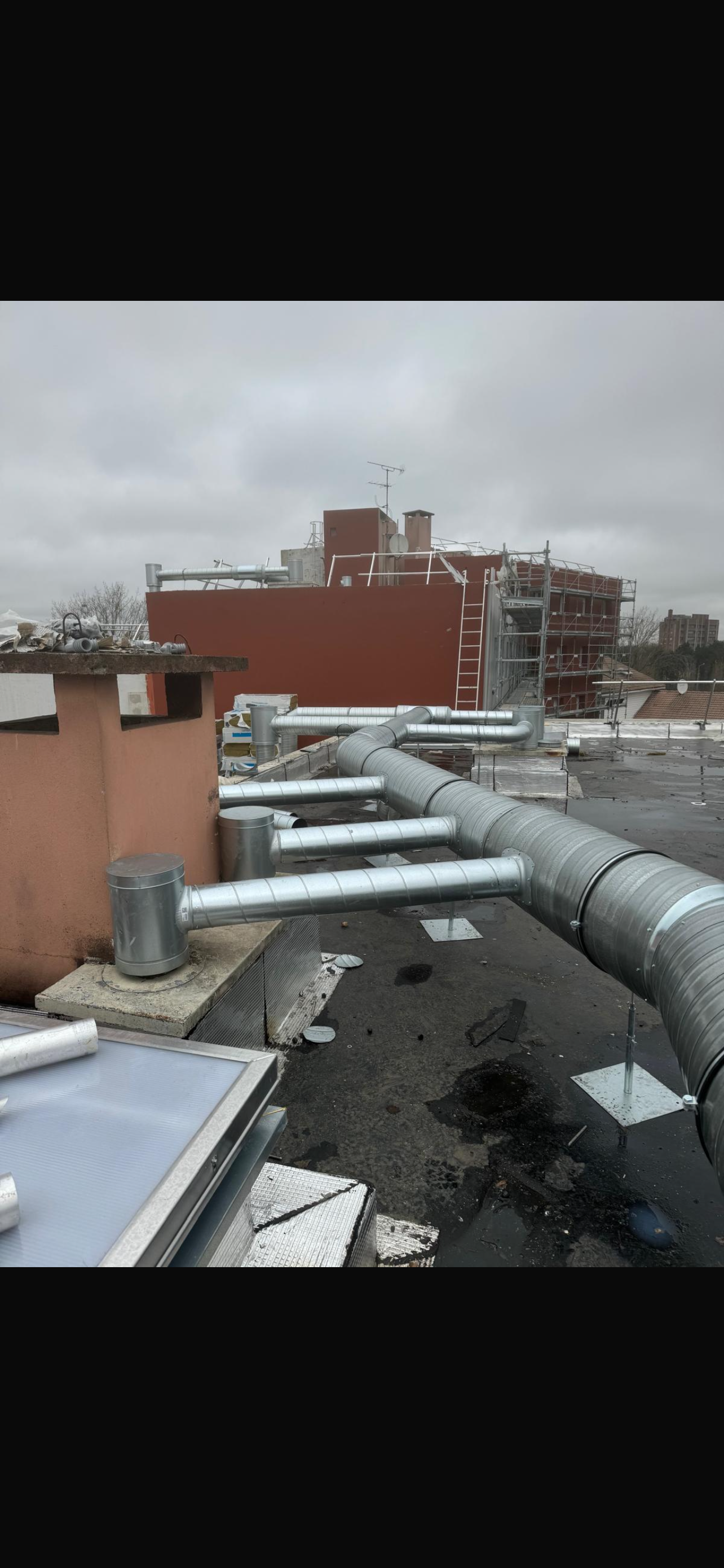 Toit-terrasse avec de grandes gaines de ventilation argentées et des bâtiments en briques rouges sous un ciel couvert